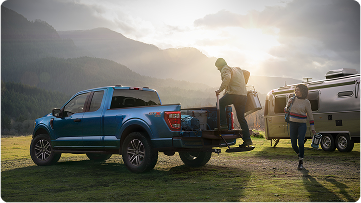 A man climbing in the bed of a Ford F-150, and a woman at a campsite with an RV in the background.